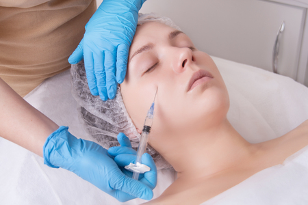 Hands of cosmetologist are close-ups that inject hyaluronic acid into cheekbone area of the girl. Real beauty treatments in spa salon.の写真素材