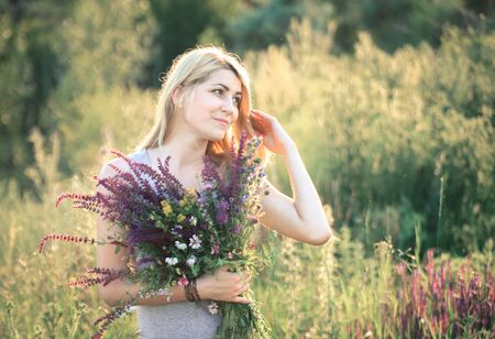 Portrait of a young beautiful woman in the nature with a bouquet of flowers in her hands.の写真素材