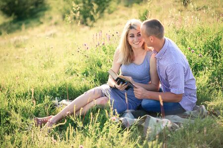 Young couple reading a book in the summer on the nature outside the city. The concept of relationships, love and relaxation.の写真素材