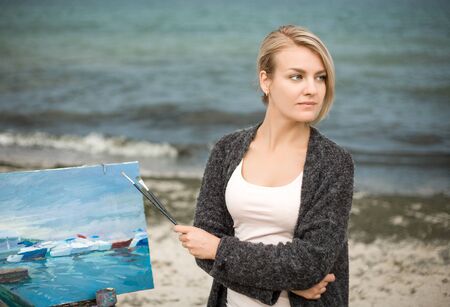 Beautiful young woman painting on the background of the sea. Beautiful portrait of the painter on outdoor.の写真素材