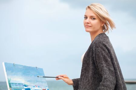 Beautiful young woman painting on the background of the sea. Beautiful portrait of the painter on outdoor.の写真素材