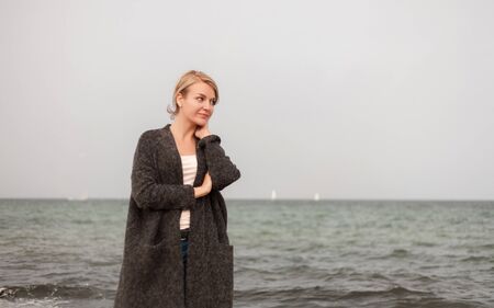 Attractive woman wearing a warm cardigan at the cold beach. Walk near sea.の写真素材