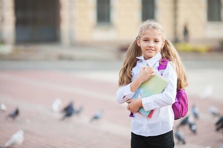 Little school girl with a backpack and book walking outdoors after lessons, education and learning concept.の写真素材