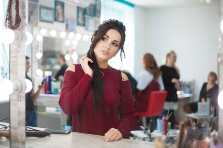 Woman in a beauty salon looks at her reflection in the mirror on her makeup and hairstyle. Real people.の写真素材