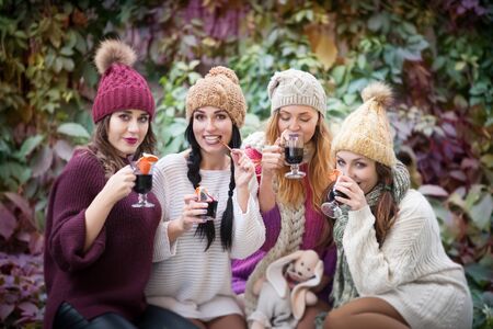Young women drink mulled wine in autumn park. Sunny autumn day. Outdoors lifestyle fashion portrait. Positive emotions.の写真素材