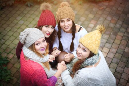 Girls in warm knitted clothes and hats hug, top view. Autumn day, a group of friends. Positive emotions.の写真素材