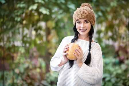 Happy lifestyle portrait of a beautiful young model in a warm autumn hat with a pumpkin in her hands.の写真素材