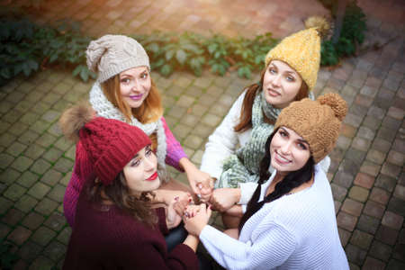 Girls in warm knitted clothes and hats hug, top view. Autumn day, a group of friends. Positive emotions.の写真素材
