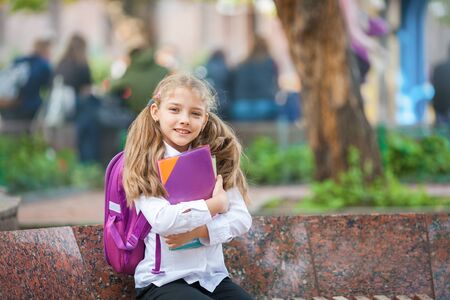 Little school girl with a backpack and book walking outdoors after lessons, read book or study, education and learning concept.の写真素材