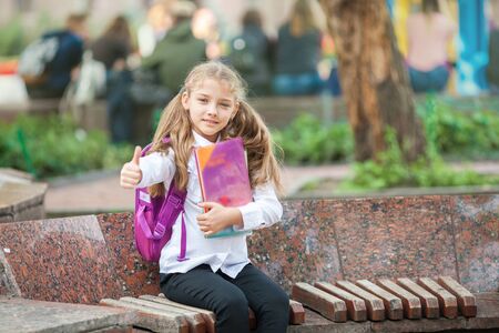 Little school girl with a backpack and book walking outdoors after lessons, read book or study, education and learning concept.の写真素材