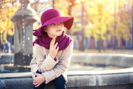 Girl in classic coat and hat in autumn park near the fountain. Autumn season, fashion, children's age.の写真素材