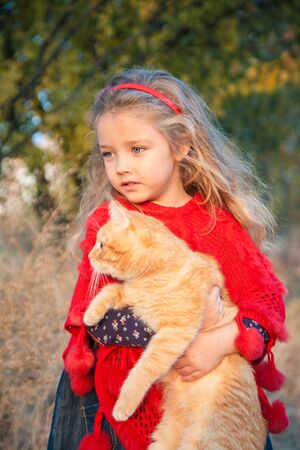 Portrait of a little girl with a red cat in her hands in autumn outdoorsの写真素材
