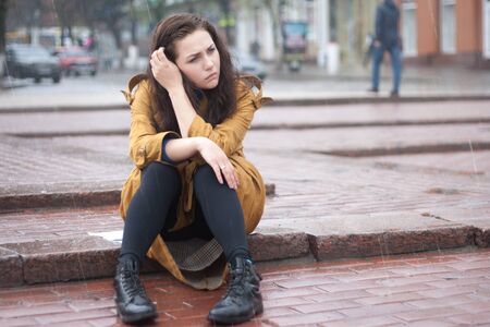 Sad woman sitting outdoors in autumn on a rainy day.の写真素材