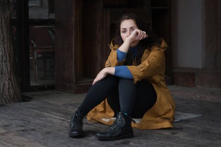 Sad woman sitting outdoors in autumn on a rainy day.の写真素材