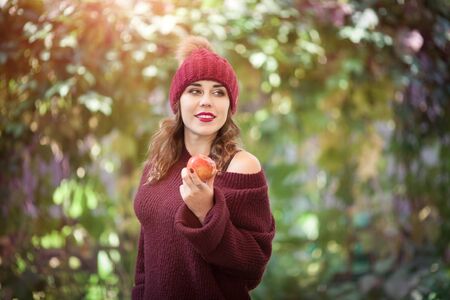 Happy lifestyle portrait of a beautiful young woman in a warm autumn hat with an apple in her hand.の写真素材