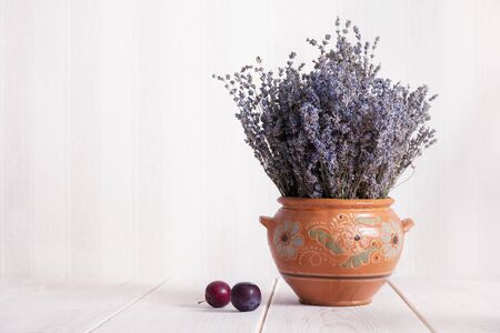 Still life with lavender in a clay jug and plums on the table. Country style.の写真素材