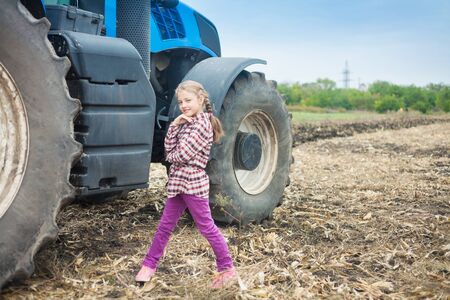 Cute girl near the modern tractor in the field. The concept of field work, agricultural machinery.の写真素材