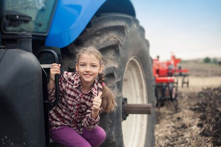 Cute girl near the modern tractor in the field. The concept of field work, agricultural machinery.の写真素材