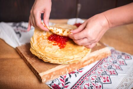 Woman wraps red caviar in a hot pancake in the kitchen, hands closeup. Rustic style, crepes close-up.の写真素材
