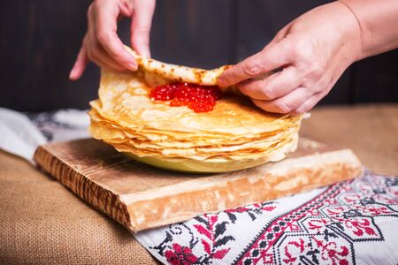 Woman wraps red caviar in a hot pancake in the kitchen, hands closeup. Rustic style, crepes close-up.の写真素材