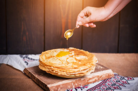 Woman pours honey on pancakes, hands closeup, home cooking.