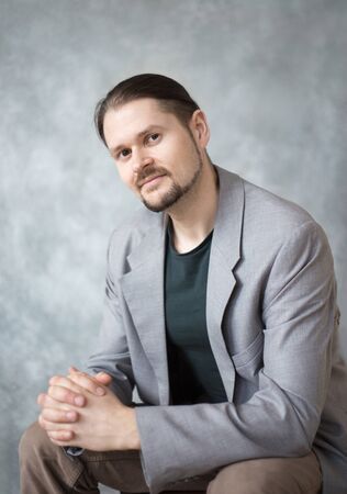 Portrait of a young man in a business jacket on a gray background in the studio. Classic portrait, casual style.の写真素材