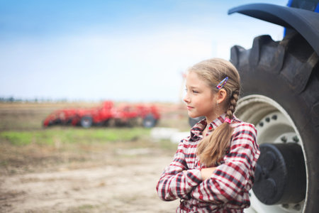 Cute girl near the modern tractor in the field. The concept of field work, agricultural machinery.の写真素材
