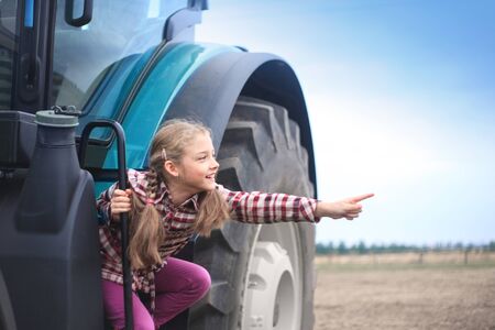 Cute girl near the modern tractor in the field. The concept of field work, agricultural machinery.の写真素材
