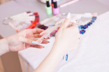 Young woman hands choosing nail color. Female manicured hands and nail color samples, beauty salon.の写真素材