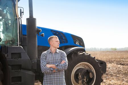 Young attractive man near a tractor. Concept of agriculture and field works.の写真素材