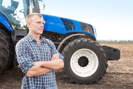 Young attractive man near a tractor. Concept of agriculture and field works.の写真素材