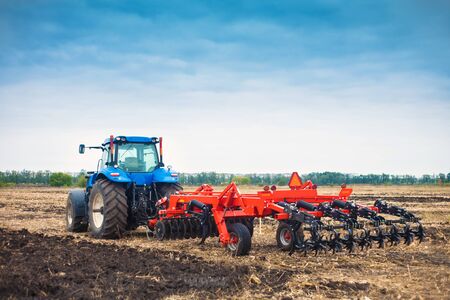 Modern tractor working in a field on a bright sunny day. The concept of work in a fields and agriculture industry.の写真素材