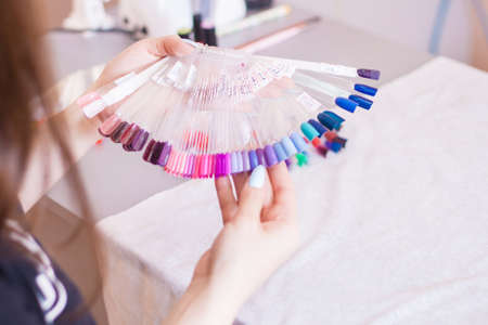 Young woman hands choosing nail color. Female manicured hands and nail color samples, beauty salon.の写真素材