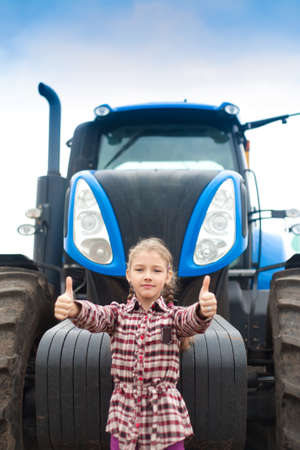 Cute girl near the modern tractor in the field. The concept of field work, agricultural machinery.の写真素材