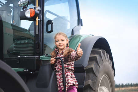 Cute girl near the modern tractor in the field. The concept of field work, agricultural machinery.の写真素材