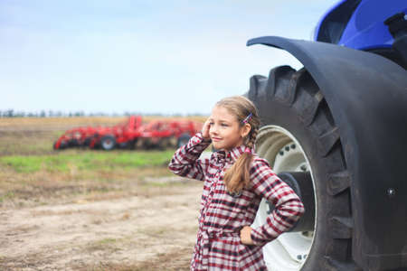 Cute girl near the modern tractor in the field. The concept of field work, agricultural machinery.の写真素材