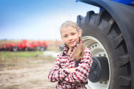 Cute girl near the modern tractor in the field. The concept of field work, agricultural machinery.の写真素材