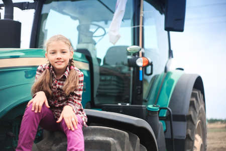 Cute girl near the modern tractor in the field. The concept of field work, agricultural machinery.の写真素材