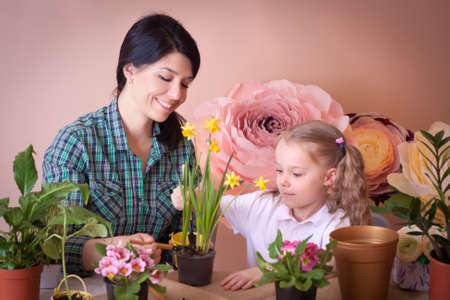 Cute child girl helps her mother to care for plants. Happy family on a studio.の写真素材