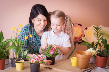 Cute child girl helps her mother to care for plants. Happy family on a studio.の写真素材