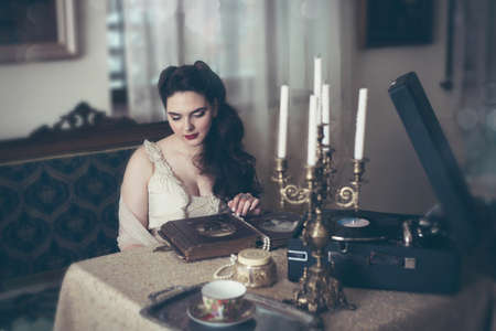 Young woman looks at a photo album. Vintage old style, retro interior.の写真素材