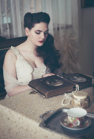 Young woman looks at a photo album. Vintage style, retro interior.