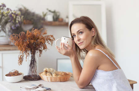 Young beautiful woman having breakfast in the morning in the kitchen.の写真素材