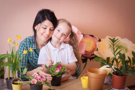 Cute child girl helps her mother to care for plants. Happy family on a studio.の写真素材