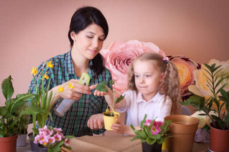 Cute child girl helps her mother to care for plants. Happy family on a studio.の写真素材