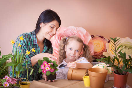 Cute child girl helps her mother to care for plants. Happy family on a studio.の写真素材