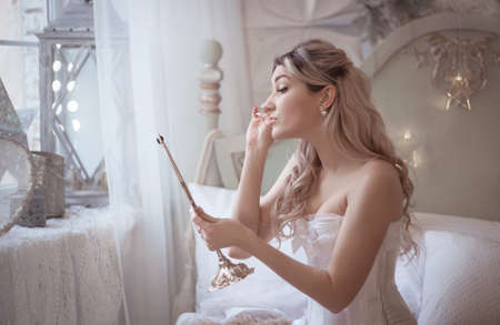 Beautiful young woman in her bedroom with a mirror. Bride's morning or vintage boudoir. Studio photo.の写真素材