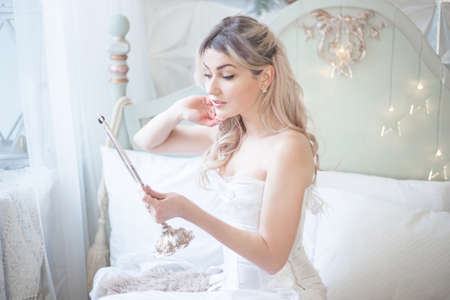 Beautiful young woman in her bedroom with a mirror. Bride's morning or vintage boudoir. Studio photo.の写真素材