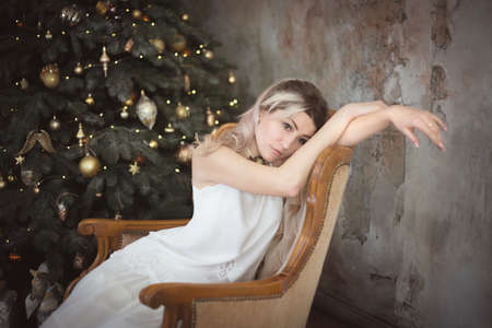 Beautiful young woman in the living room near the Christmas tree. Brooding or lonely, retro style. Studio photo.の写真素材