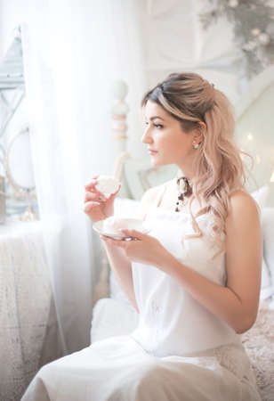 Cute young woman eating sweets in the morning in the bedroom. Gentle winter morning. Studio photo.の写真素材